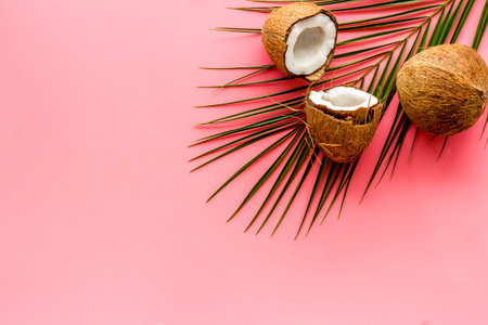 Exotic background with coconuts and palm leaves on pink background top-down.
