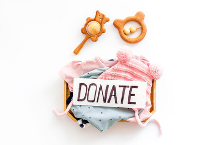 Donate text. Box with clothes for kids on white background top-down.