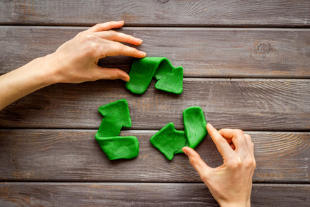 Recycling symbol composition with hands on dark wooden background top-down