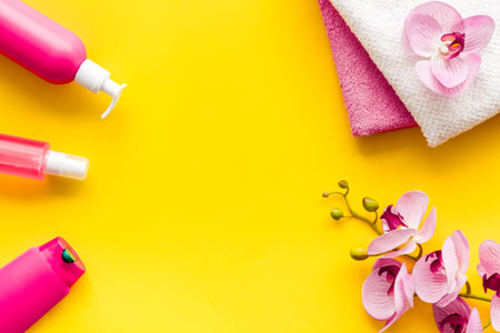 Hair care set with shampoo and towel - pink - on yellow background top-down.