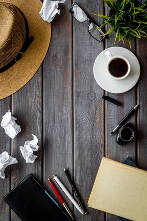 Writer's desk with notebook, hat and crumpled paper on dark wooden background top-down.の写真素材