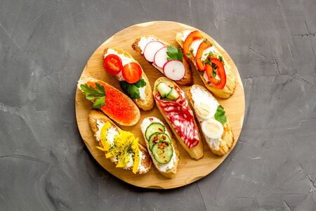 Set of bruschetta on cutting board on grey background top-down.