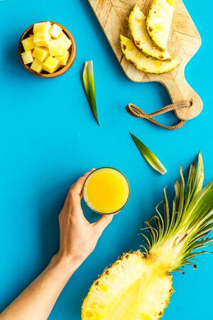 Pineapple juice in hands near sliced fruits on blue background top-down.の写真素材