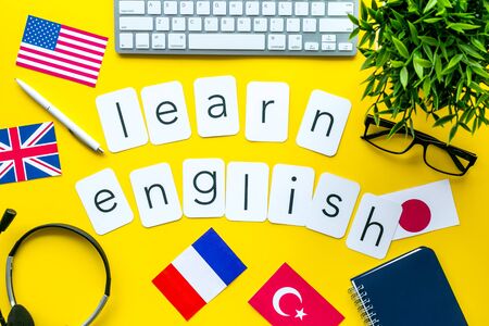 Learn English online. Concept with text, headset and keyboard on yellow background top-down.