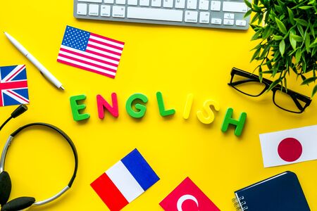 Learn English online. Concept with text, headset and keyboard on yellow background top-down.