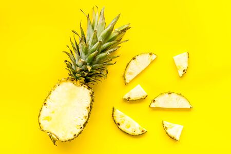 Pineapple - half of fruit and slices - on yellow background top-down.