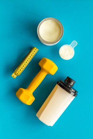 Sport nutrition. Whey protein, shaker, dumbbells on blue background top-down flay lay.の写真素材