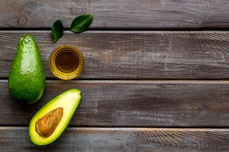 Avocado oil - for cooking - in glass bowl near halfs of vegetable on wooden background top-down frame copy spaceの写真素材