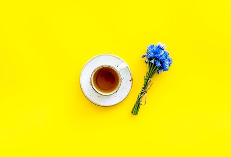 Summer tea party. Cup near cornflowers bouquet on yellow background top-down.の写真素材