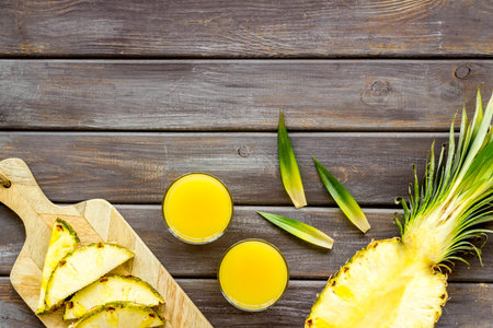 Pineapple juice on wooden table with half of fruit top-down.
