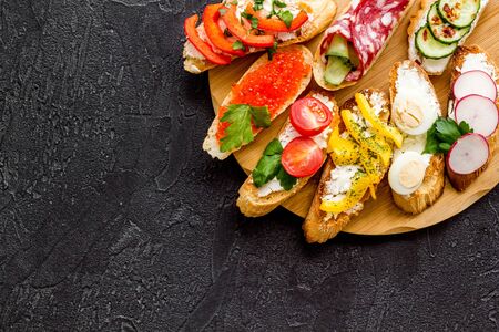 Set of bruschetta on cutting board on black background top-down.の写真素材
