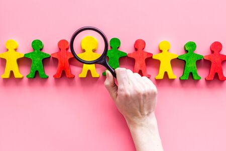 Wooden figures of people under black magnifying glass on pink table. Recruitment, hiring, leadership concept.の写真素材
