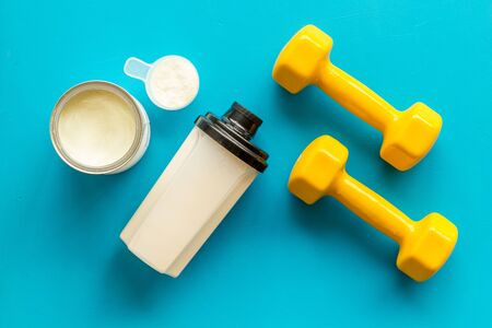 Sport nutrition. Whey protein, shaker, dumbbells on blue background top-down flay lay.の写真素材