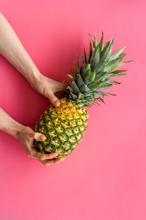 Pineapple in hands on bright pink background top-down copy spaceの写真素材