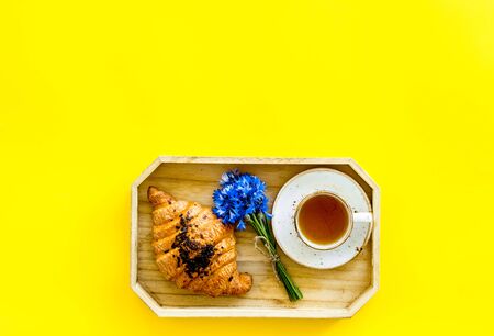 Breakfast with summer flowers. Tea, croissant and cornflowers on yellow background top-down.の写真素材