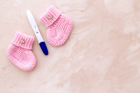 Positive pregnancy test. Baby girl concept with pink booties on beige background top-down copy space