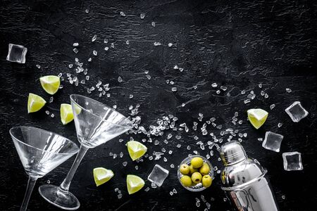 Bar background with martini glasses, shaker, ice, lemon and olives on black table top-down.の写真素材
