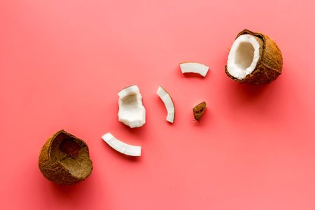 Cut coconuts - halfs and pieces - on pink background top-down.