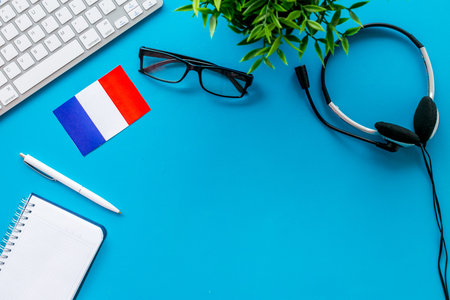 Learn French online. Concept with flag, headset and keyboard on blue background top-down.