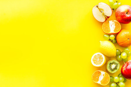 Fresh fruits background with citruses, apple, kiwi and grape on yellow table top-down.