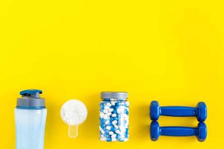 Creatine capsules, protein near shaker and dumbbells - sports supplements - flat lay on yellow background top viewの写真素材