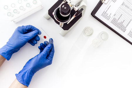Research with microscope, hands hold blood sample. White table top view copy space