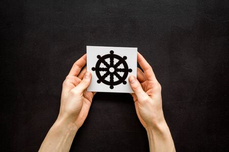 Wheel of dharma Buddhist religion symbol in hands on black table top viewの写真素材
