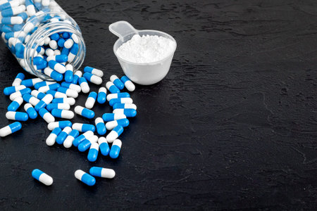 Creatine capsules and protein in scoop on black background copy space