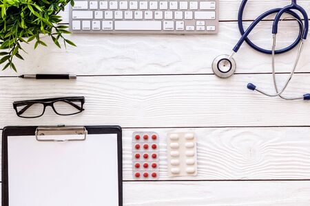 Doctor desk with pills, tablet, stethoscope. White wooden table top-down space for textの写真素材
