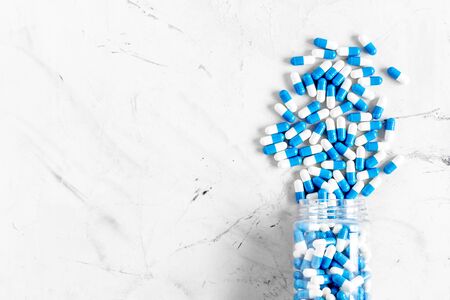 Blue and white capsules poured from a bottle - sports supplement creatine - on white background top...