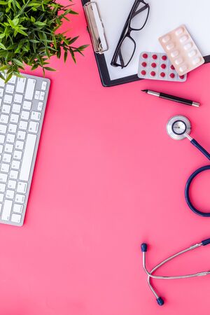 Doctor desk with pills, tablet, stethoscope. Pink table top-down space for textの写真素材