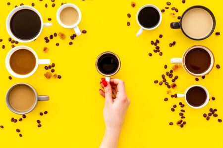 Coffee addiction. Mug in hand, many cups on yellow desk from aboveの写真素材