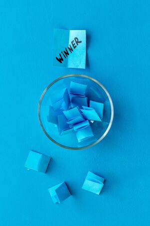 Winner selection. Paper pieces for lottery in vase on blue table from aboveの写真素材