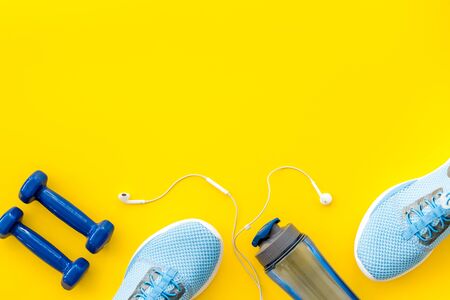 Fitness accessories. Dumbbells and sneakers on yellow table top view copy spaceの写真素材