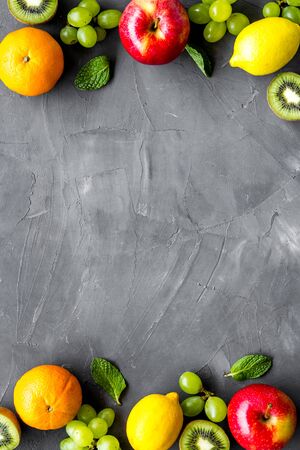 Oranges, lemon, apple, kiwi and grape - healthy food concept with fruits - on grey background top-down frame copy spaceの写真素材