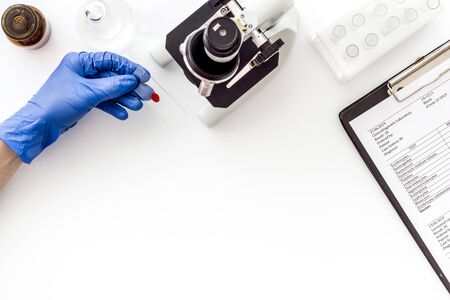Clinical science research with microscope. Hand holds blood sample on white background top view.