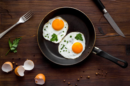 Fried eggs on frying pan on wooden background top view.