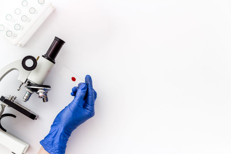 Clinical science research with microscope. Hand holds blood sample on white background top view copy...