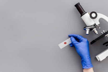 Clinical science research with microscope. Hand holds blood sample on grey background top view copy...