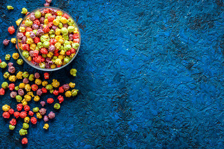 Colored popcorn in bowl on blue background top view copy space