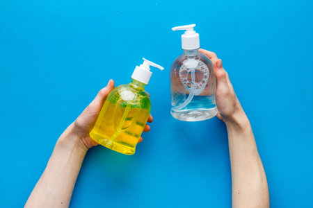 Sanitizer bottle in hands - coronavirus prevention - on blue background top view