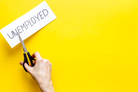 Employment, new job concept. Hands cut paper -unemployed - on yellow desk from above space for text