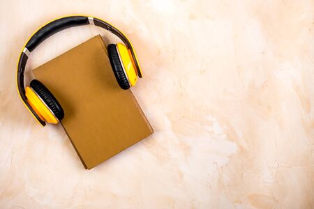 Book and yellow headphones on. Beige background top view.の写真素材