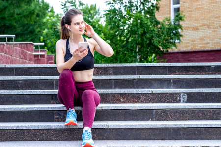 Listening to music after sport training. Girl on stairs outdoor