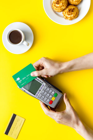 Payment transactions. Hand hold card near terminal on yellow cafe table top-down