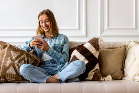 Young woman with mobile phone on sofa at homeの写真素材