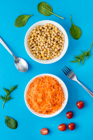 Vegetarian meal. Chickpeas and carrot in bowls on blue table top viewの写真素材