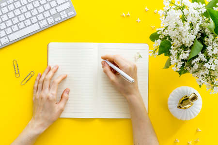 Female hands writing on notebook. Workplace with flowers bouquet top viewの写真素材