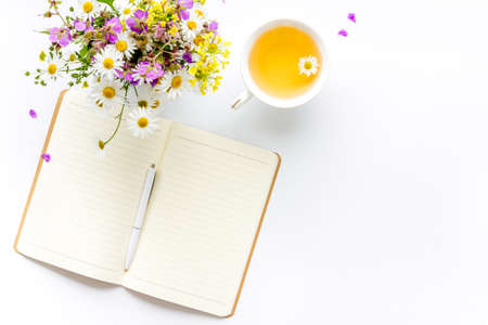 Bouquet of wild summer flowers with tea and open notepad. Above view.の写真素材