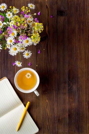 Bouquet of wild summer flowers with tea and open notepad. Above viewの写真素材